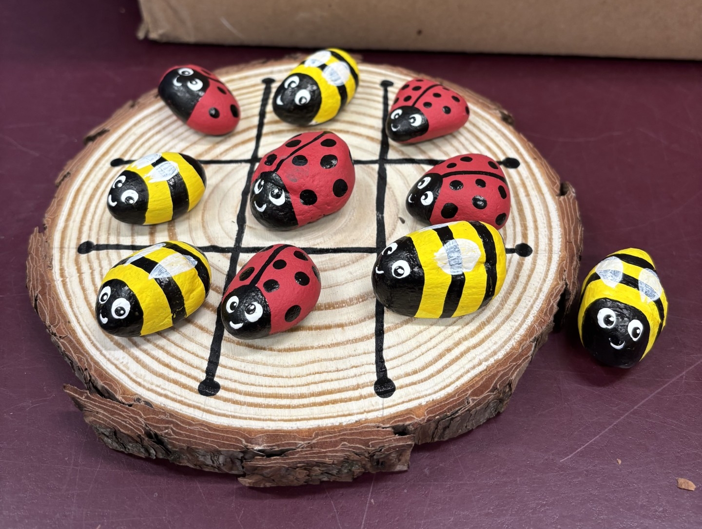 Wood circle tic-tac-toe with painted rocks of ladybugs and bees